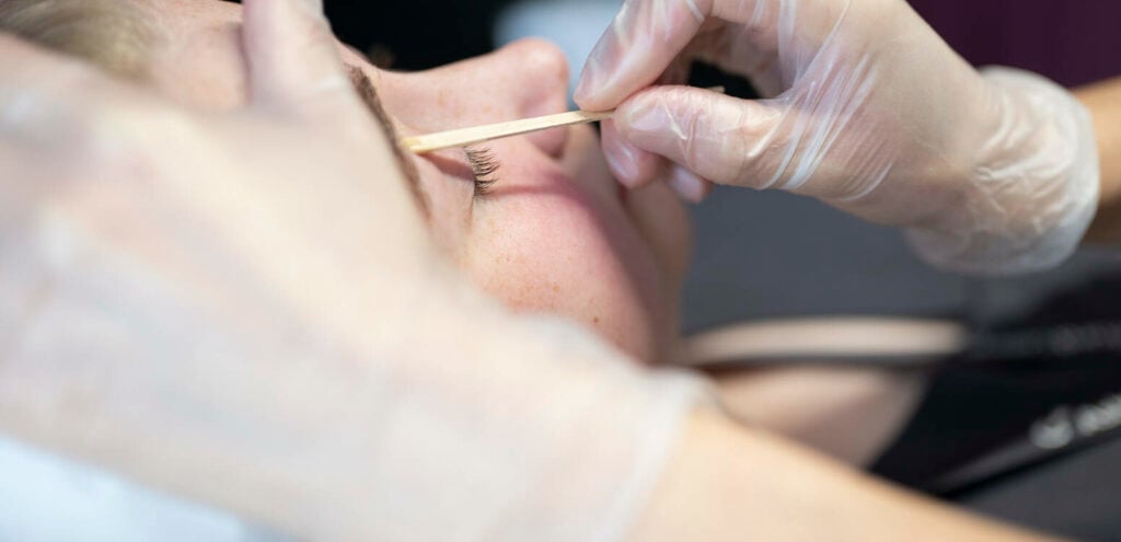 Beauty student waxing a clients eyebrow.