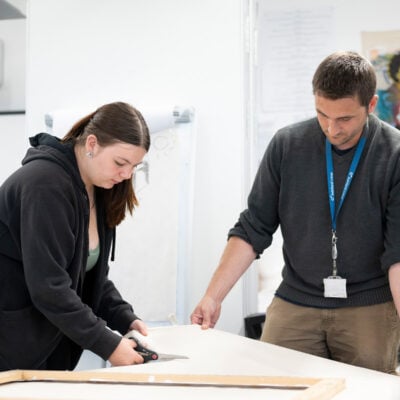 Art and design student cutting with staff memeber Paul heping.