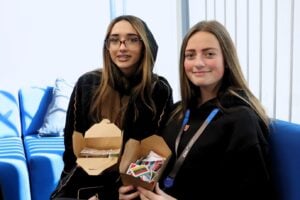 2 students holding boxes filled with stickers of world flags