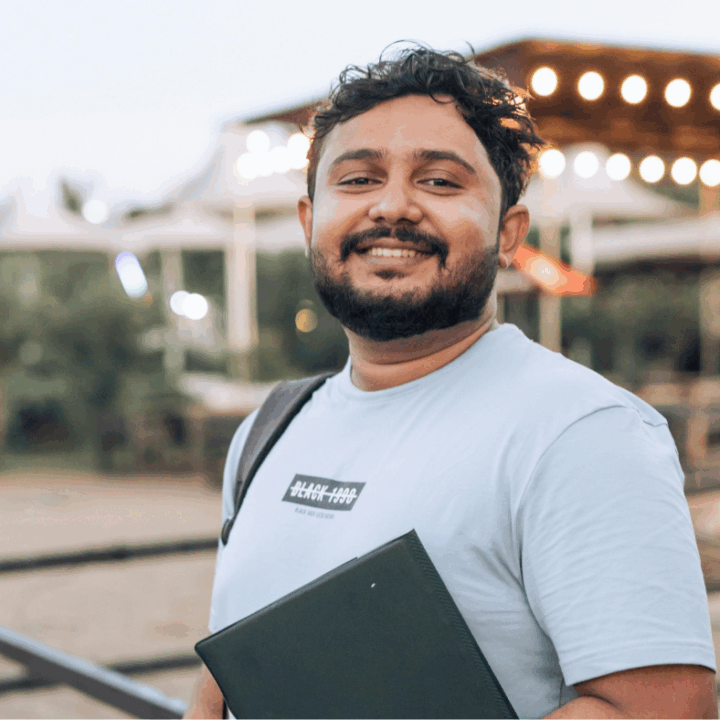 Adult man smiling at camera outside carrying a laptop and a bag.