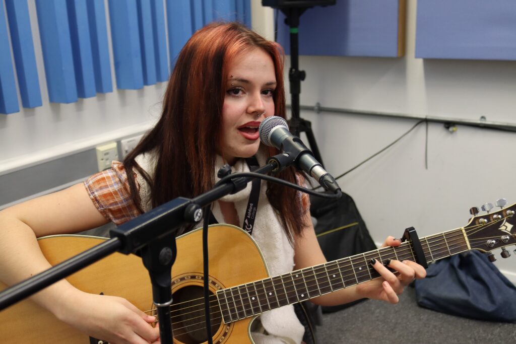 Kiah in a practice room, singing and playing guitar