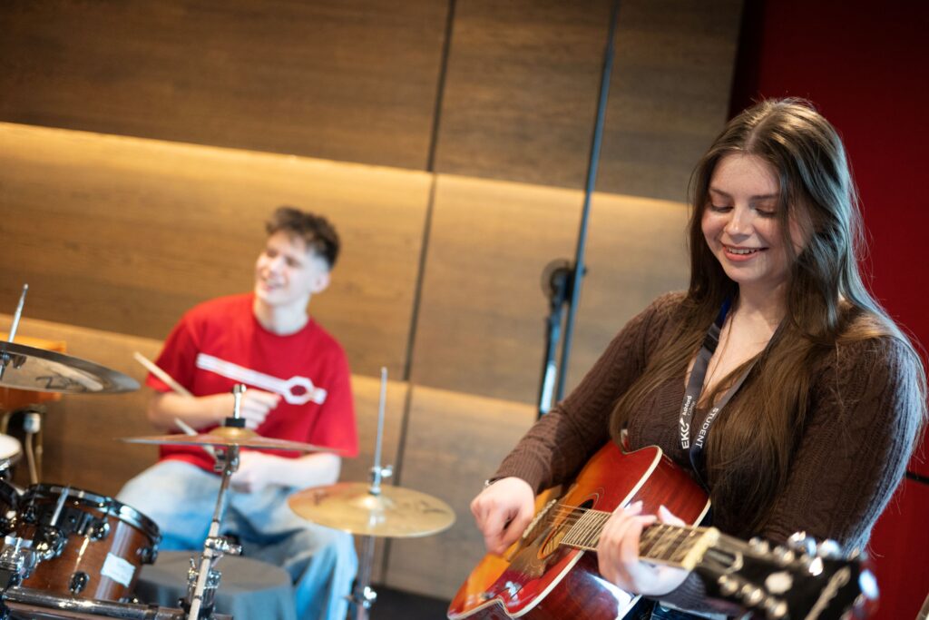 two students, one playing a guitar on playing the drums