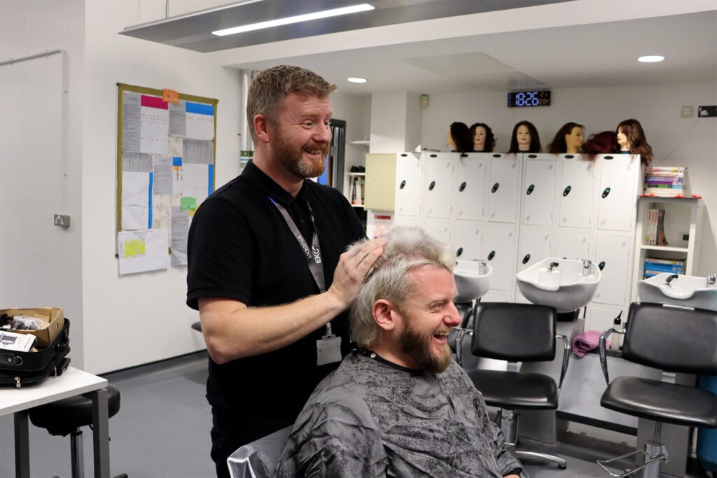 male student styling the hair of a barbering client