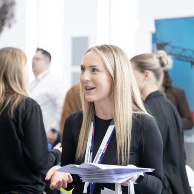 student talking to another student, she has long blonde hair and is holding paper