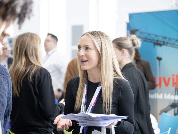 student talking to another student, she has long blonde hair and is holding paper