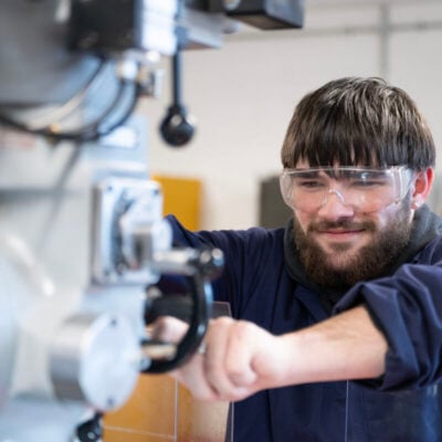 student wearing eye protection using engineering equipment and smiling.