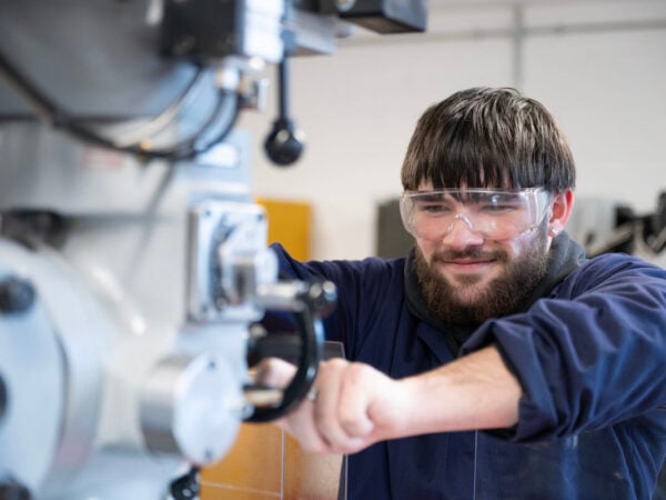 student wearing eye protection using engineering equipment and smiling.