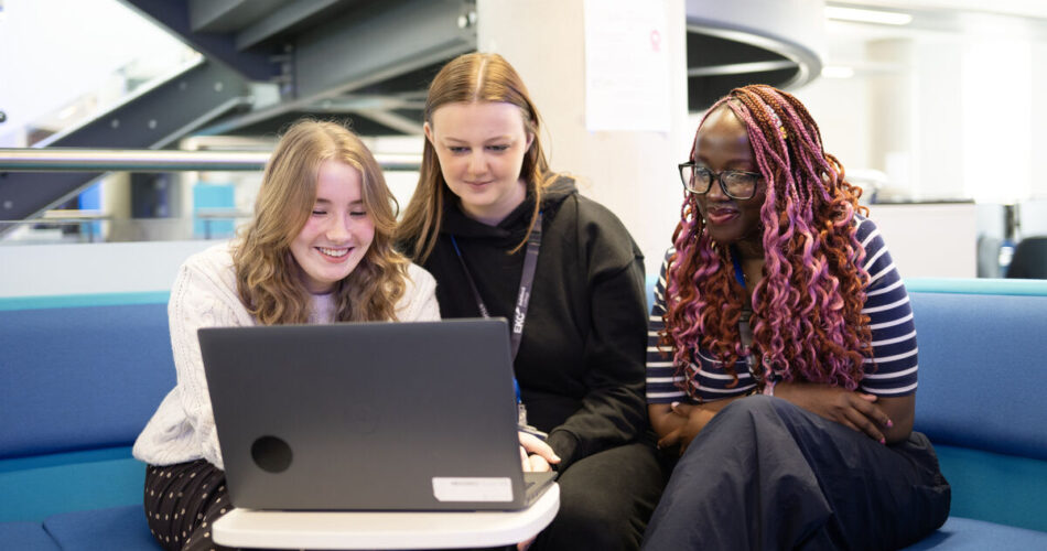 Three students sitting together smiling and looking at a laptop