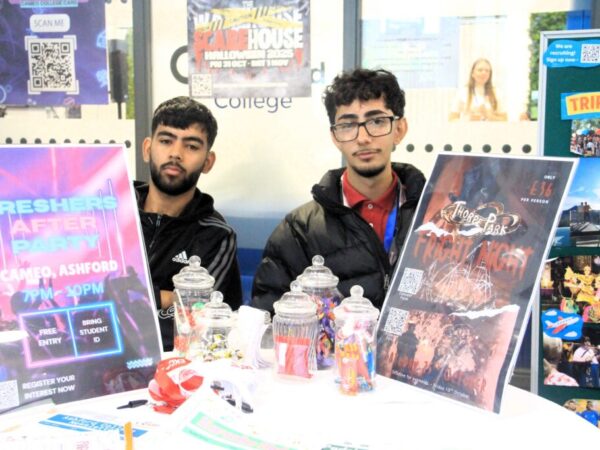 two students sitting behind a table at a freshers fayre with different information on the table for students