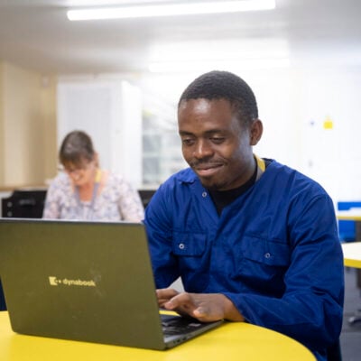 adult student smiling and working on a laptop at a table.