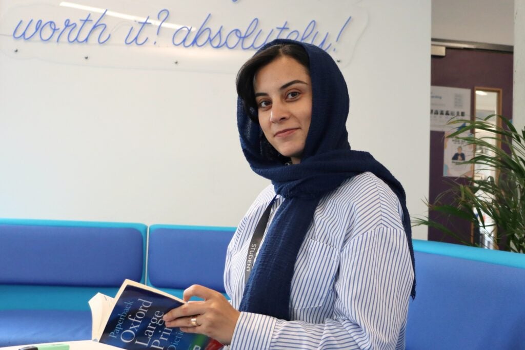 adult student with head scarf looking at the camera, sitting down holding a dictionary