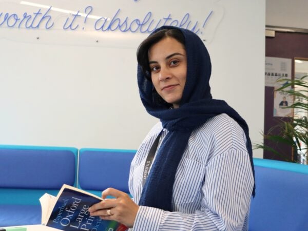 adult student with head scarf looking at the camera, sitting down holding a dictionary