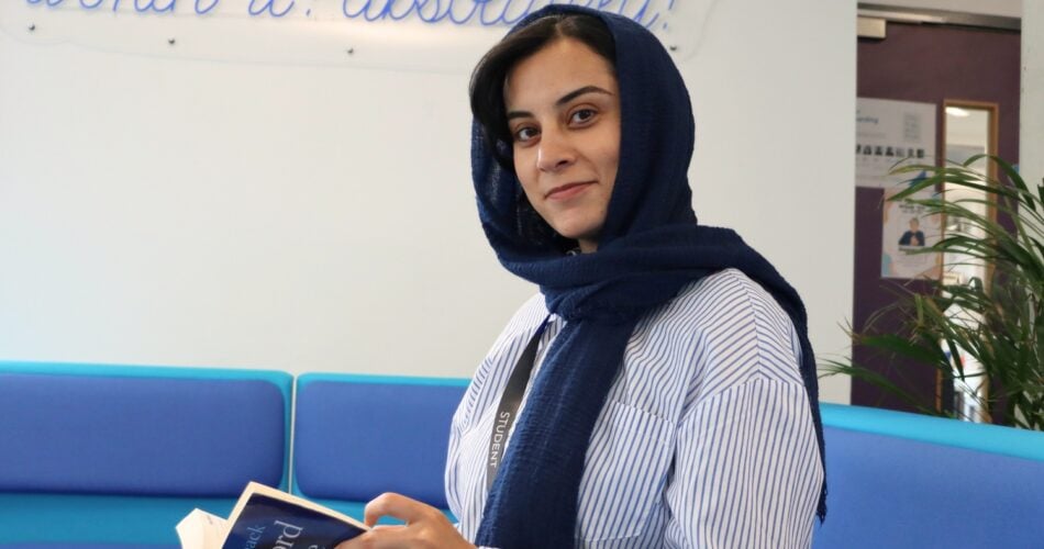 adult student with head scarf looking at the camera, sitting down holding a dictionary