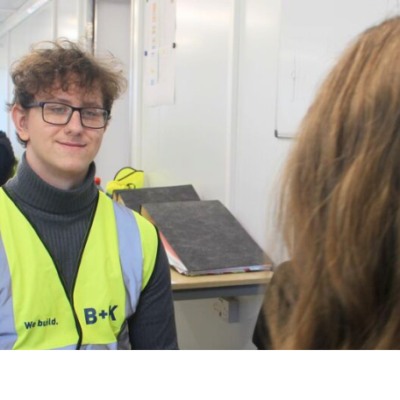 student on work experience in a building site office talking to a woman.