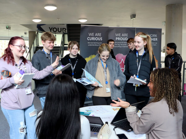 a group of students talking to adults around a desk at the college for careers fair