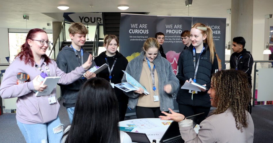 a group of students talking to adults around a desk at the college for careers fair