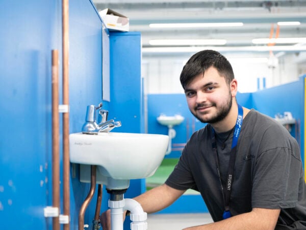 plumbing student looking at camera whilst working on a sink attached to a blue wall