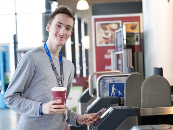 Student looking at the camera whilst scanning their ticket to get through the barrier at the train station.