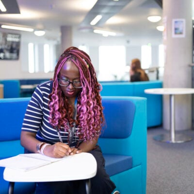 Student sitting at a table writing in a book in the e-hub area
