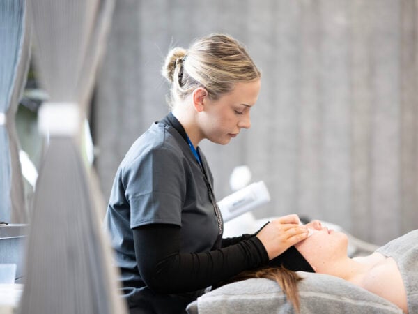 students putting cotton pads on a clients eyes as she lies on a massage table