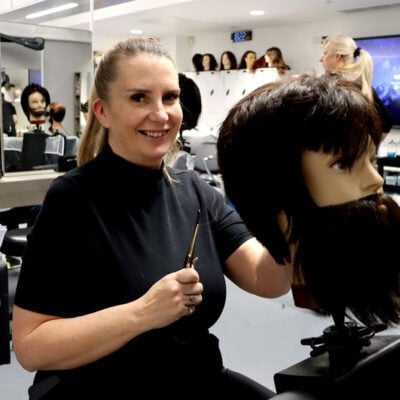 barbering student holding a pair of scissors and cutting hair on a mannequin