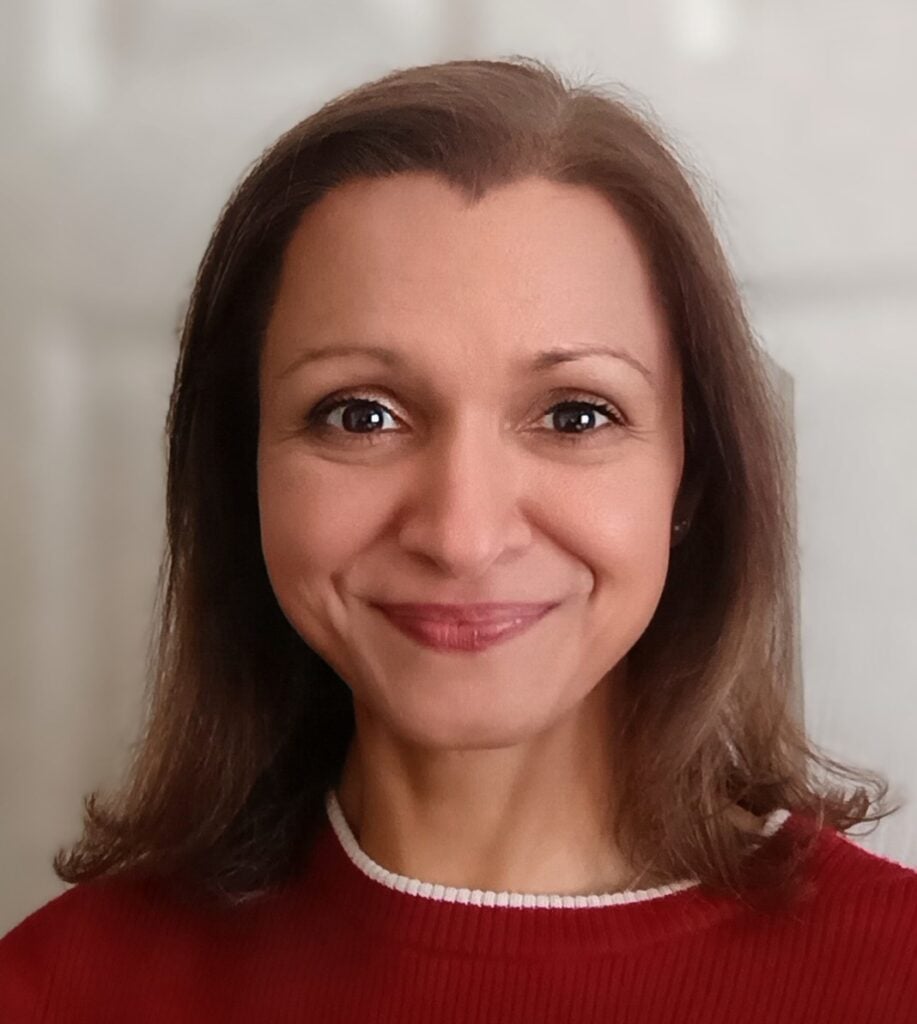 Woman in a red top with brunette shoulder length hair smiling at camera.