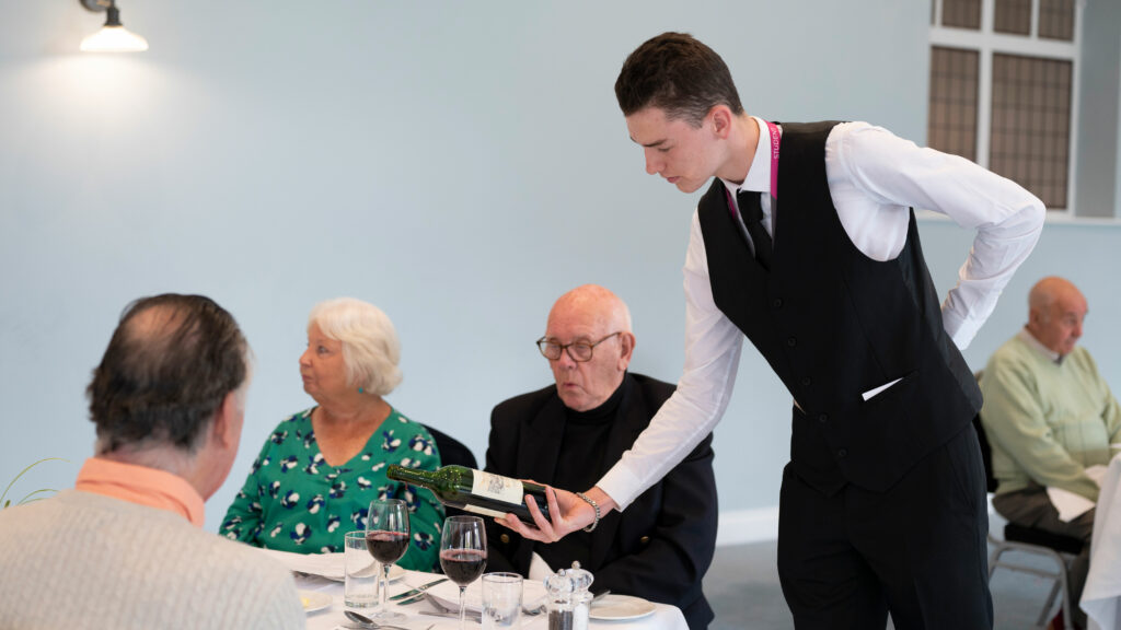 Hospitality student pouring wine for customers