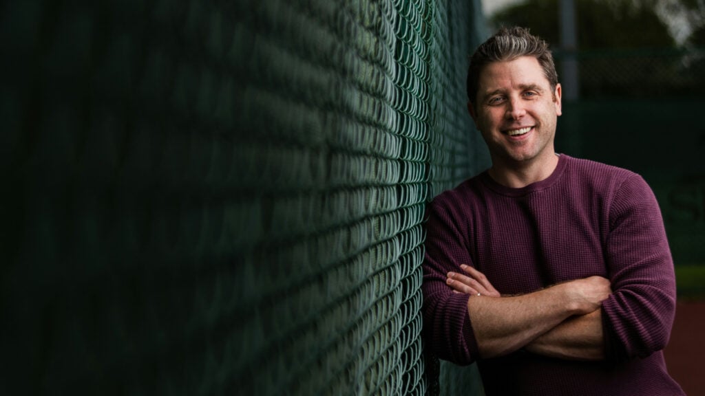 Adult leaning against a fence looking happy