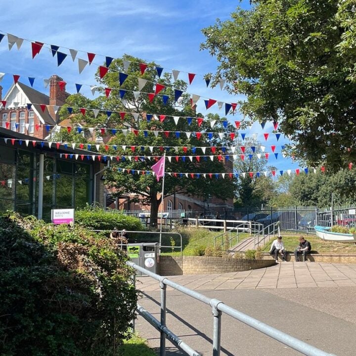 Photo of outside space including trees, bushes and path leading to a building. A few benches and places to sit are visible.
