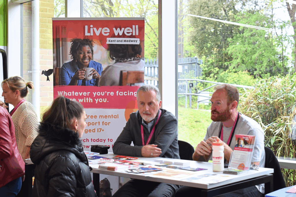 a student sits at a table with two men at a park life event