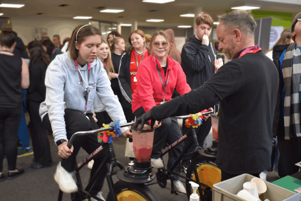 a female student rides an exercise bike to power a blender.