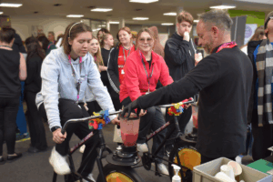 a female student rides an exercise bike to power a blender.