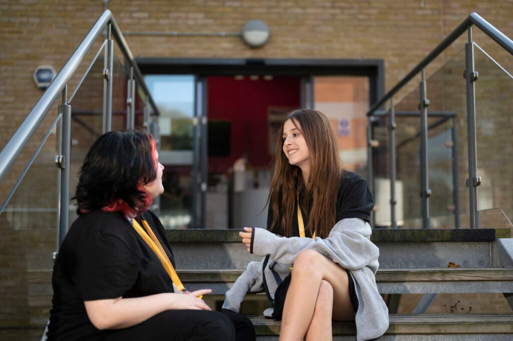 2 students sitting on steps outside a college