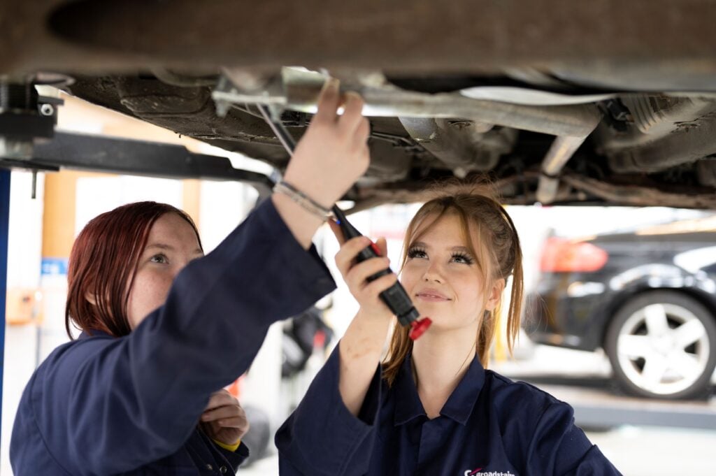 Two students working under a car on a ramp