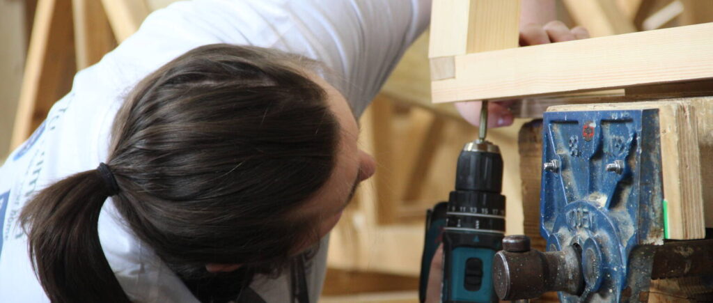 Student drilling a hole into a piece of wood underneath.