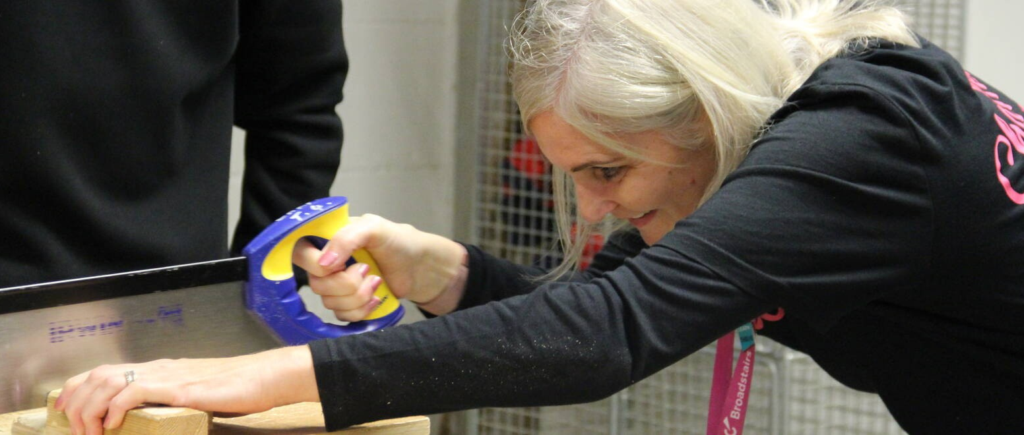 staff sawing a piece of wood on a workbench