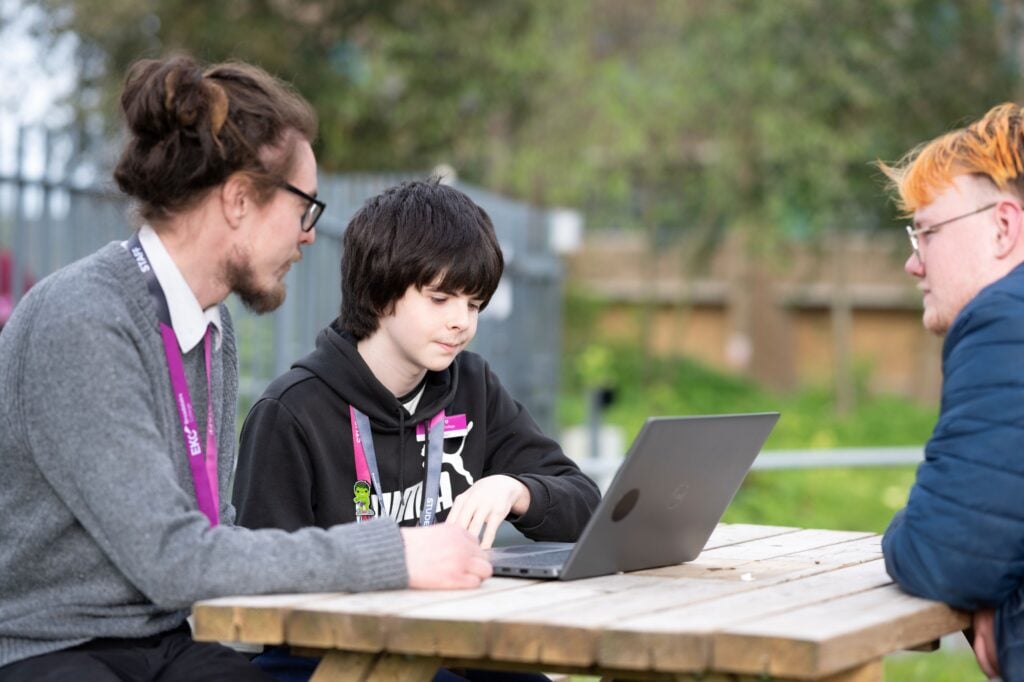 tutor sat at a picnic bench with a learner looking at a laptop