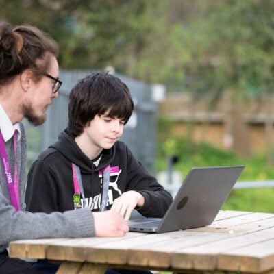 tutor sat at a picnic bench with a learner looking at a laptop