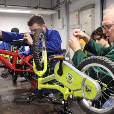 students working on small bikes on a worktop with blue aprons on.