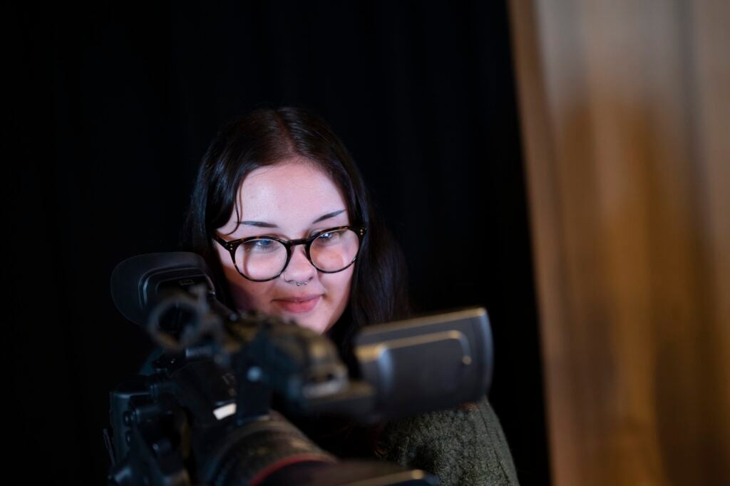 creative media student looking at a video camera