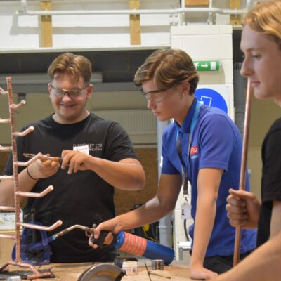 students smiling and putting pipes together to create a christmas tree