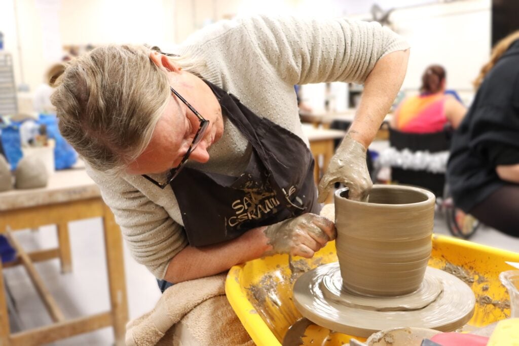 Lady using clay on a wheel to make a pot