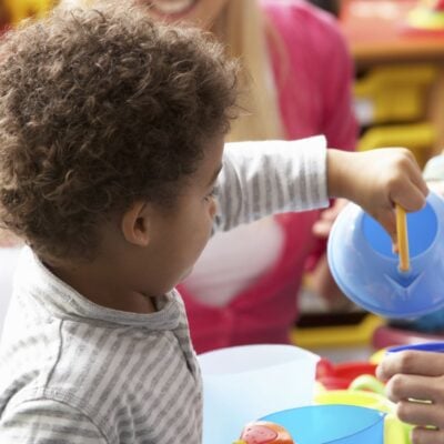 Child pretending to pour water from a plastic toy kettle