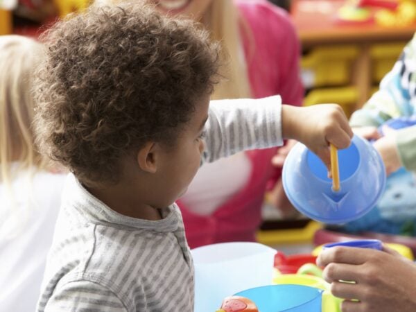 Child pretending to pour water from a plastic toy kettle