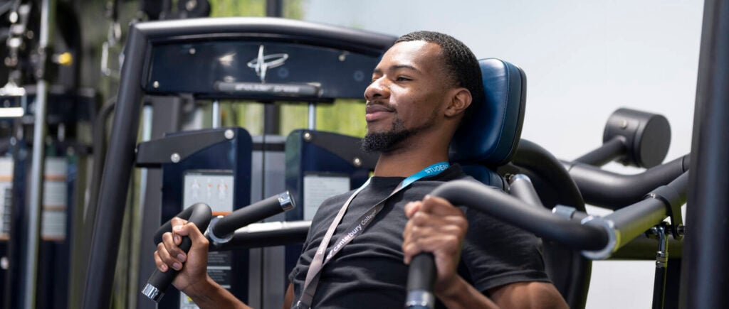 Male fitness coach student using weighted machine in gym