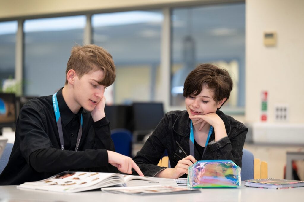 two students look at a book at college