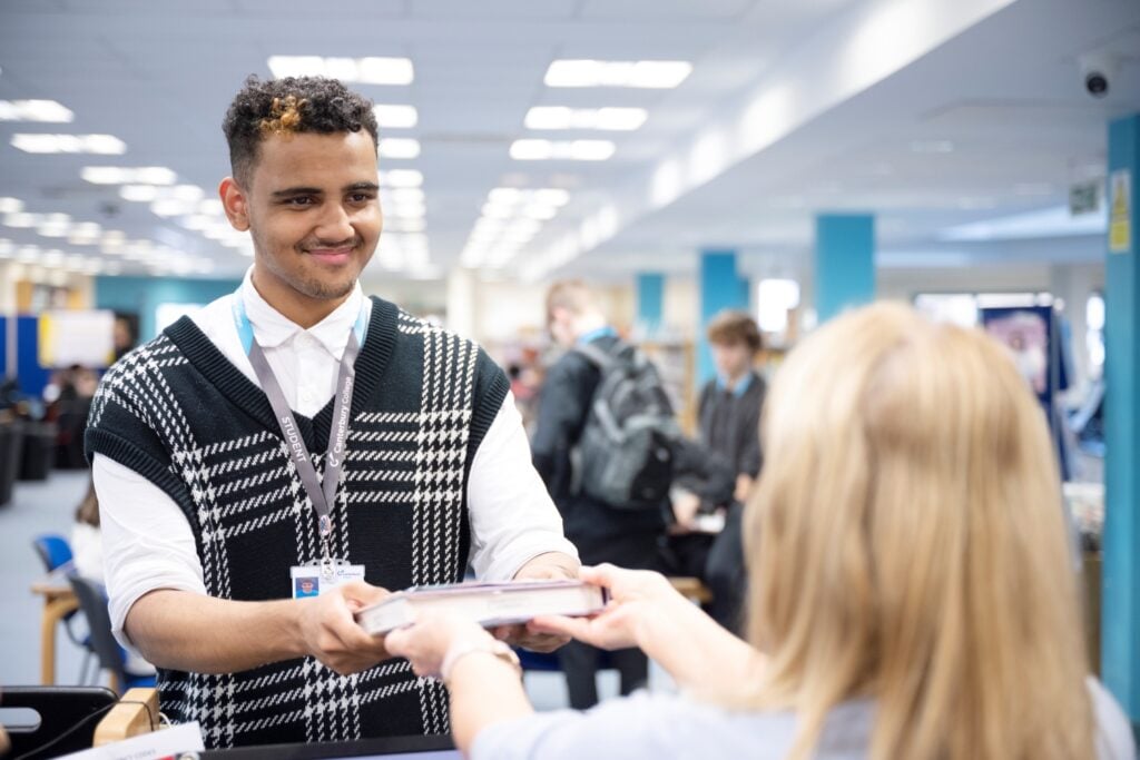 male presenting student returns a book at the College library