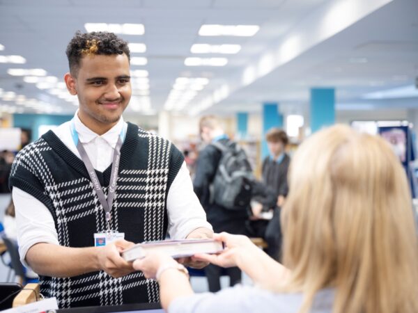 male presenting student returns a book at the College library