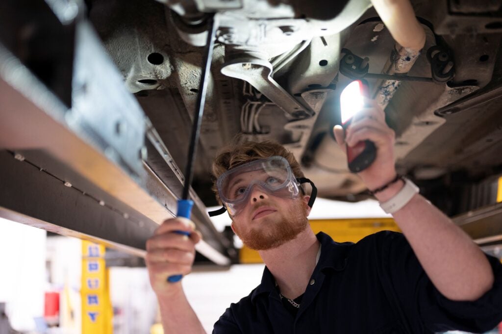 Student working under a car that is on a ramp