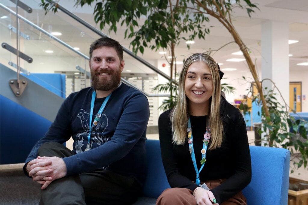 2 people sat on a sofa smiling at the camera